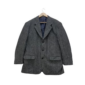 May include: A gray herringbone blazer with a notched lapel, three-button closure, and two front pockets. The blazer is hanging on a wooden hanger against a white background. The interior lining is navy blue.