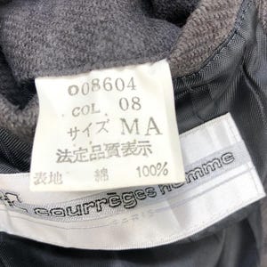 May include: A white tag with black text that reads "008604", "COL. 08", "サイズ MA", "法定品質表示", "綿 100%". Below the tag is a white tag with black text that reads "courreges homme PARIS".