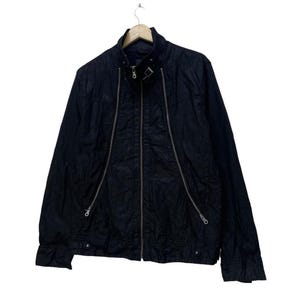 May include: A black jacket with a stand-up collar and silver zippers. The jacket has a full-length zipper down the front and two diagonal zippers on the chest. The jacket is hanging on a wooden hanger.