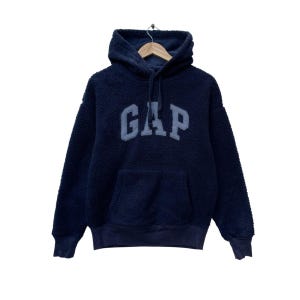 Puede incluir: Una sudadera con capucha de color azul marino de tejido polar con un gran logotipo "GAP" bordado en la parte delantera. La sudadera tiene capucha con cordón y bolsillo canguro.