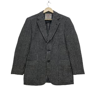 May include: A black and white houndstooth patterned blazer with a single button closure and two pockets. The blazer has a label that reads "Harris Tweed."