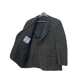 May include: A tweed blazer in a houndstooth pattern, featuring shades of brown, green, and blue. The jacket is open, revealing a dark lining and a label with text. The blazer is hanging on a wooden hanger.