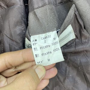 May include: A brown jacket with a label that reads "C48632", "2", "M", "Polyester 100%", "Polyester 100%", "M".