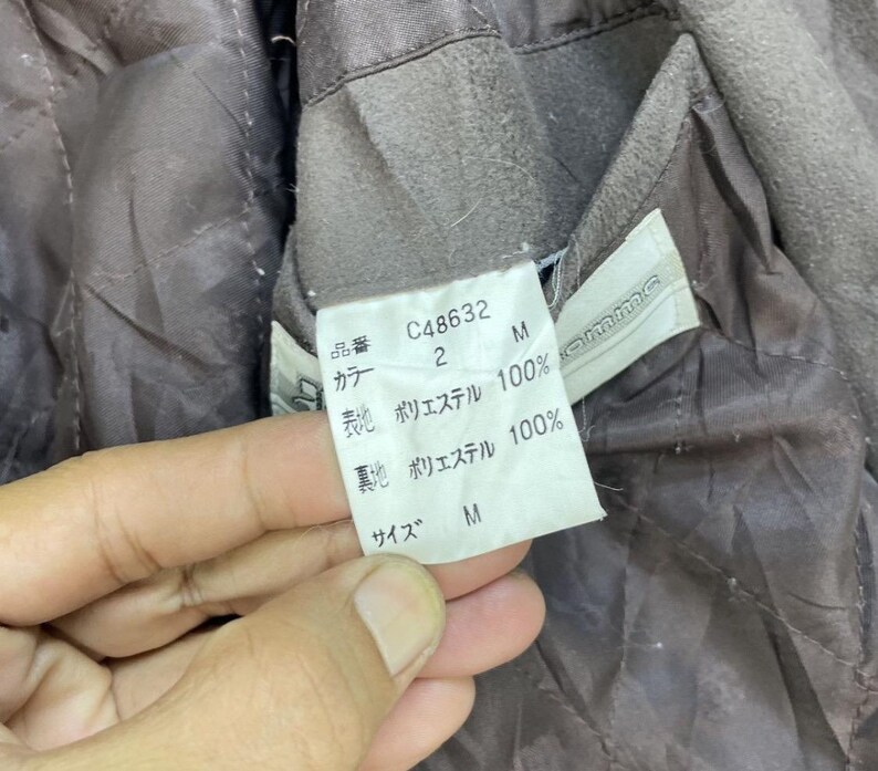 May include: A brown jacket with a label that reads "C48632", "2", "M", "Polyester 100%", "Polyester 100%", "M".