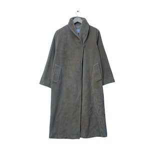 Puede incluir: Abrigo largo verde oliva con cuello ancho y cierre de un solo botón. El abrigo tiene dos bolsillos delanteros y mangas largas. Cuelga de una percha de madera sobre un fondo blanco.