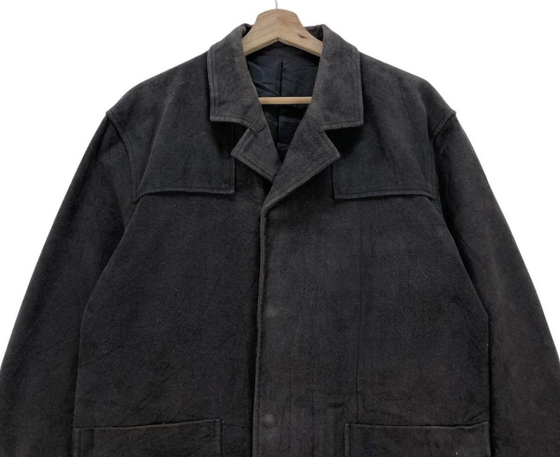 May include: A dark gray long-sleeved jacket with a button-up front and two pockets. The jacket has a collar and a slightly textured fabric.