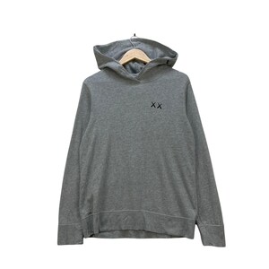 Peut inclure: Un sweat &agrave; capuche gris avec une capuche et des manches longues. Le sweat &agrave; capuche porte un petit logo noir "XX" sur la poitrine. Le v&ecirc;tement est suspendu &agrave; un cintre en bois.