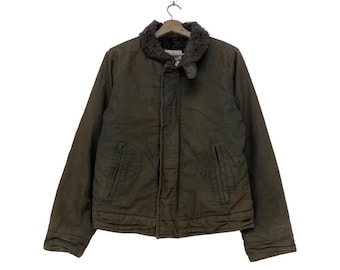May include: A dark green jacket with a brown faux fur collar and zipper closure. The jacket has two pockets on the front and a zippered pocket on the left sleeve.