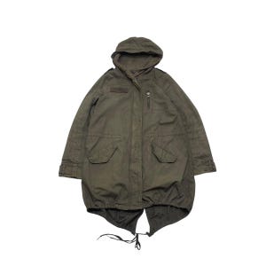 May include: An olive green parka with a hood, front pockets, and a zipper closure. The jacket has a drawstring at the bottom and a small patch on the chest. The parka is a vintage style.