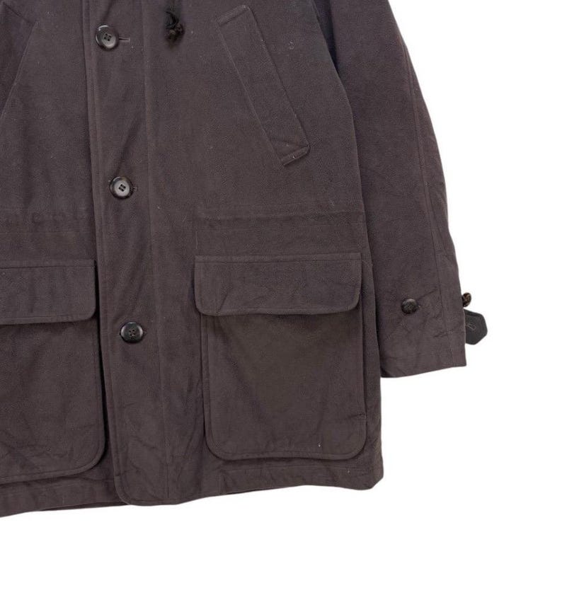 May include: A dark gray hooded jacket with a button closure, two large pockets on the front, and two smaller pockets on the chest. The jacket has a flap on the left sleeve.