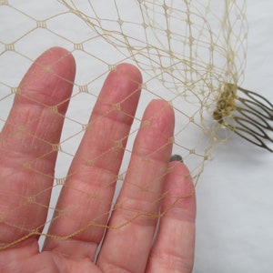 May include: A beige bridal veil with a delicate diamond pattern and a gold comb attached.