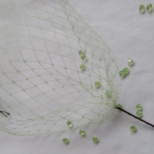 May include: A white tulle veil with a single hair comb attached. Green glass beads are scattered around the veil.