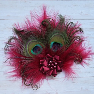 May include: A burgundy feather hair clip with two peacock feathers and a burgundy bow with a pearl center.