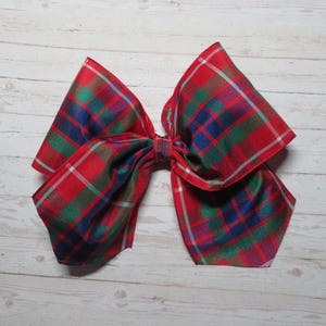 May include: A large red, green, blue, and white plaid bow. The bow is made of a silky fabric and is tied in a classic bow shape.
