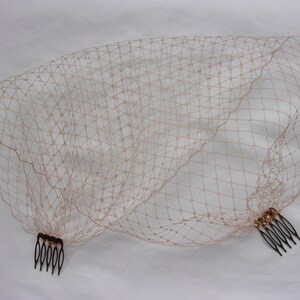 May include: A blush-colored bridal veil with a fine mesh pattern and two combs attached.