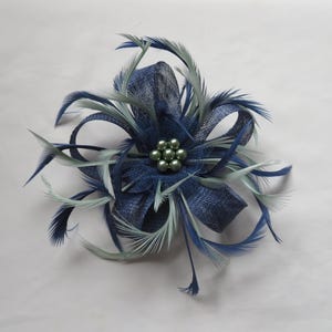 May include: A navy blue and light green fascinator with a central cluster of small, round beads. The headpiece features layered fabric and delicate feathers in shades of blue and green, creating a floral design.