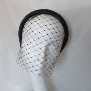 May include: Black headband with a black tulle veil attached. The veil is a diamond pattern and covers the face.