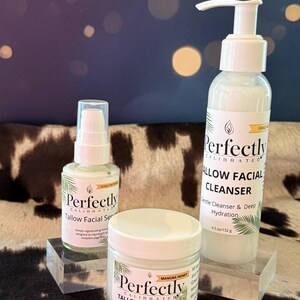 May include: Three white skincare products with green accents are displayed on clear blocks. The products include a facial serum, face cream, and facial cleanser. The labels read "Perfectly Calibrated" and "Tallow Facial" with additional text.