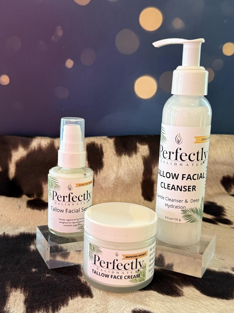 May include: Three white skincare products with green accents are displayed on clear blocks. The products include a facial serum, face cream, and facial cleanser. The labels read "Perfectly Calibrated" and "Tallow Facial" with additional text.