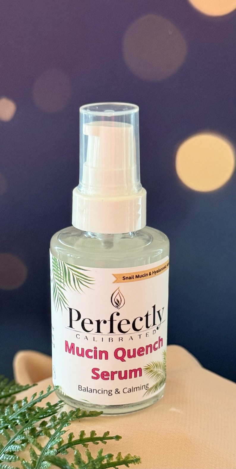 May include: A clear glass bottle of Perfectly Calibrated Mucin Quench Serum with a white pump dispenser. The label includes text and palm frond illustrations. The serum is for balancing and calming the skin.