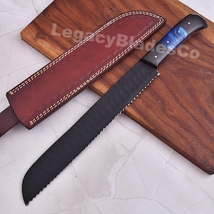 May include: A black serrated bread knife with a blue and black handle rests on a wooden cutting board. A brown leather sheath with white stitching is next to the knife. The text "LegacyBladesCo" is visible.