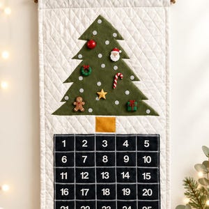 May include: A quilted white fabric wall hanging featuring a green felt Christmas tree decorated with small ornaments including a gingerbread man, candy cane, and Santa face, positioned above a black grid calendar numbered from 1 to 25.