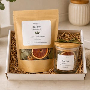 May include: A spa day gift set in a white box. The set includes a kraft paper bag and a glass jar, both labeled "Spa Day." The bag contains dried citrus slices and eucalyptus. The jar also contains dried citrus slices. A wooden bowl with citrus slices is in the foreground.