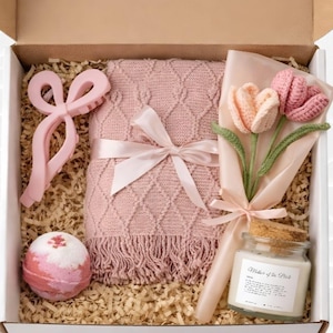 Op de afbeelding: Een geschenkdoos gevuld met een roze deken, een roze haarclip, een badbruisbal, een boeket gehaakte tulpen en een kaars. De kaars heeft een kurken deksel en een label met "Mother of the Bride".
