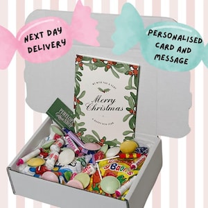 Puede incluir: Una caja blanca llena de caramelos coloridos y una tarjeta de Navidad que dice "Merry Christmas". La caja está decorada con gráficos en forma de caramelos rosas y azules que dicen "Next Day Delivery" y "Personalised Card and Message".