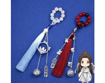 May include: Two decorative tassels with beaded loops. One has a light blue tassel with a silver lotus pendant and a white beaded loop. The other has a red tassel with a silver butterfly pendant and a red beaded loop. Both have silver accents.