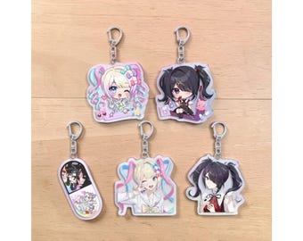 May include: Five acrylic keychains with anime-style character designs. Each keychain features a different character with colorful hair and outfits. The keychains are attached to silver key rings and are on a light brown wooden surface.