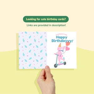 May include: A birthday card held by a hand, featuring a pink bunny on a scooter with balloons and the text "Happy Birthdayyy!". The card's interior has a pattern of blue feathers and pink hearts. The text "Looking for cute birthday cards? Links are provided in description!" is also visible.