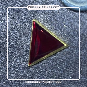 May include: A red triangle pin with a gold border. The pin is on a gray textured surface.