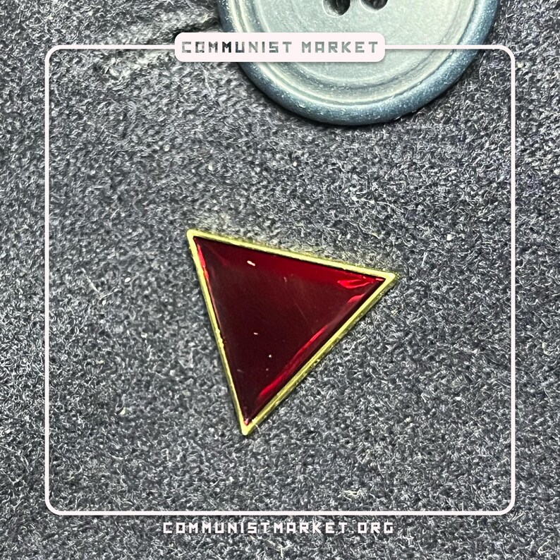 May include: A red triangle pin with a gold border. The pin is on a dark gray fabric background.