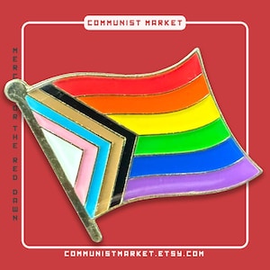 Op de afbeelding: Een metalen emaille speld in de vorm van een wapperende vlag met het Progress Pride-ontwerp. De vlag bevat horizontale strepen in rood, oranje, geel, groen, blauw en paars, met een chevron in zwart, bruin, lichtblauw, roze en wit.