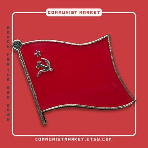 Op de afbeelding: Een rode emaille pin met een gestileerde afbeelding van de vlag van de Sovjet-Unie met een hamer en sikkel en een gouden ster. De pin is zilverkleurig en heeft een licht gebogen vorm.