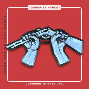 Könnte beinhalten: Eine silberne Emaille-Anstecknadel, die zwei Hände zeigt, die ein Gewehr halten. Die Nadel hat eine goldene Nadelrückseite. Der Text "COMMUNIST MARKET" befindet sich oben im Bild und "COMMUNISTMARKET.ORG" unten.