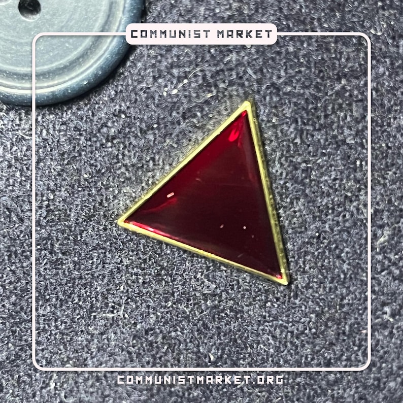 May include: A red triangle pin with a gold border. The pin is on a gray textured surface.