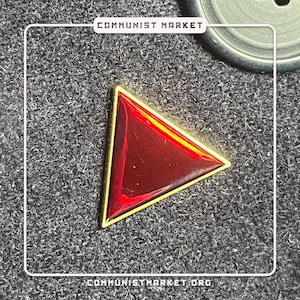 May include: A red triangle pin with a gold border. The pin is on a black fabric background.