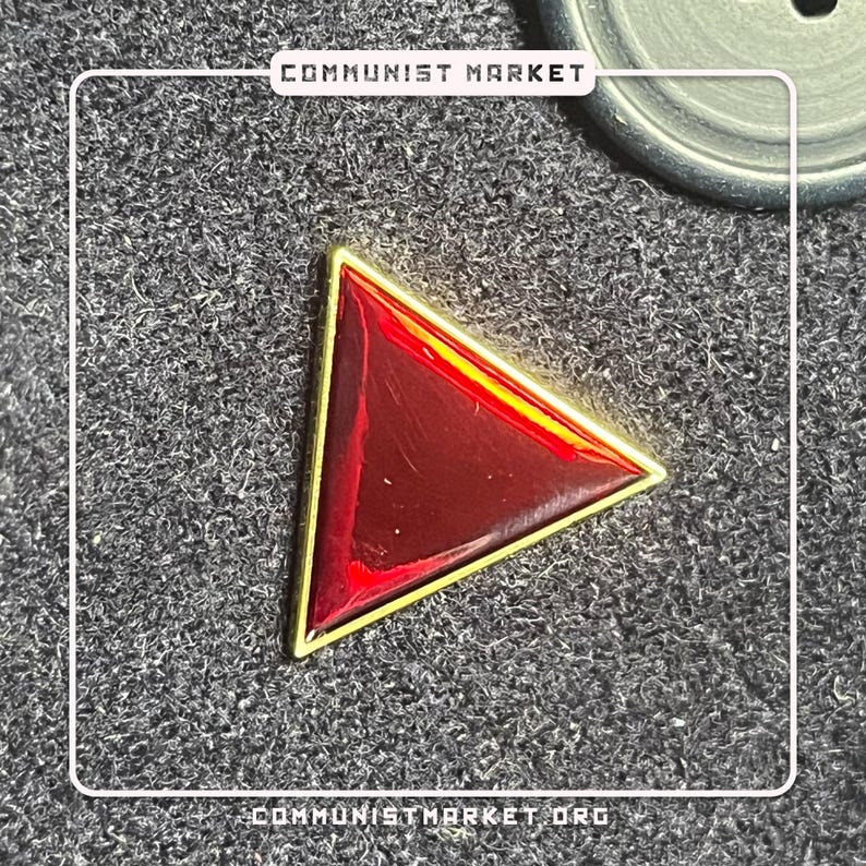 May include: A red triangle pin with a gold border. The pin is on a black fabric background.