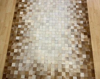 May include: A brown and white patchwork cowhide rug with a square pattern. The rug is made of individual pieces of cowhide that have been sewn together.