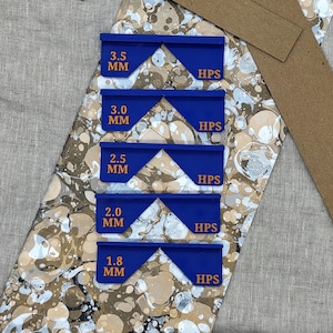 May include: A close-up of five blue, geometric tools with the text "3.5 MM", "3.0 MM", "2.5 MM", "2.0 MM", and "1.8 MM". Each tool has the text "HPS". The tools are on a patterned surface.
