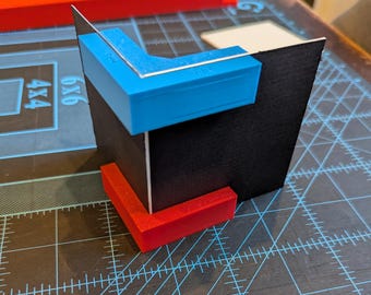 May include: A black cardboard box with a blue and red plastic corner brace. The brace is attached to the box with a screw.