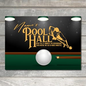 May include: A black and gold sign with the text "Jame's Pool Hall" and the tagline "Open till it annoys the neighbours... Then maybe we go 10 more minutes." A silhouette of a person playing pool is shown on the sign. A green felt pool table with a white billiard ball and a pool cue is shown in the foreground.
