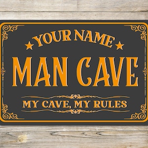 May include: A black and orange sign with the text "YOUR NAME MAN CAVE MY CAVE, MY RULES" in a decorative font.