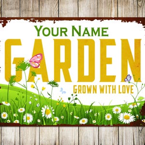 May include: A white metal sign with a rusty brown border. The sign has a green and yellow garden scene with the text "YOUR NAME GARDEN GROWN WITH LOVE".