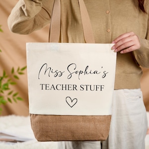 May include: Cream-colored tote bag with the text "Miss Sophia's TEACHER STUFF" in black script, a heart symbol, and a brown bottom. The bag has beige handles.