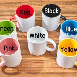 Peut inclure: Une collection de tasses en c&eacute;ramique blanches avec des int&eacute;rieurs et des poign&eacute;es color&eacute;s. Les tasses sont &eacute;tiquet&eacute;es avec les couleurs : rouge, noir, bleu, vert, rose, jaune et blanc. Les tasses sont dispos&eacute;es sur une surface en bois.