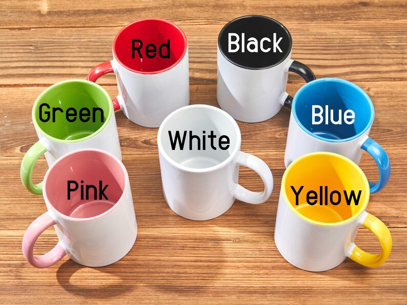 Peut inclure: Une collection de tasses en c&eacute;ramique blanches avec des int&eacute;rieurs et des poign&eacute;es color&eacute;s. Les tasses sont &eacute;tiquet&eacute;es avec les couleurs : rouge, noir, bleu, vert, rose, jaune et blanc. Les tasses sont dispos&eacute;es sur une surface en bois.