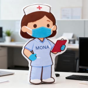 Puede incluir: Muñeca de enfermera de peluche con uniforme azul claro, gorro blanco con cruz roja y mascarilla azul. La muñeca sostiene una carpeta roja y tiene el nombre "MONA" impreso en la camisa. La muñeca está sobre un escritorio blanco.